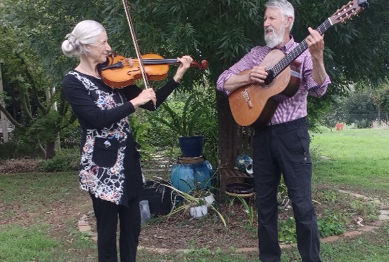 Leonie-Ruth and David Acland playing a violin and guitar on their permaculture farm, Tanglewood.