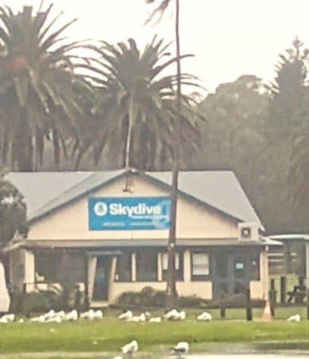 Front entrance of a skydiving school with clear signage, set against the backdrop of the Illawarra Escarpment and Pacific Ocean. A place where novice skydivers prepare for their first leap, symbolizing the safe, supportive space provided by a mentor for personal and professional growth. Ideal setting for learning to take life's big leaps with confidence and guidance.